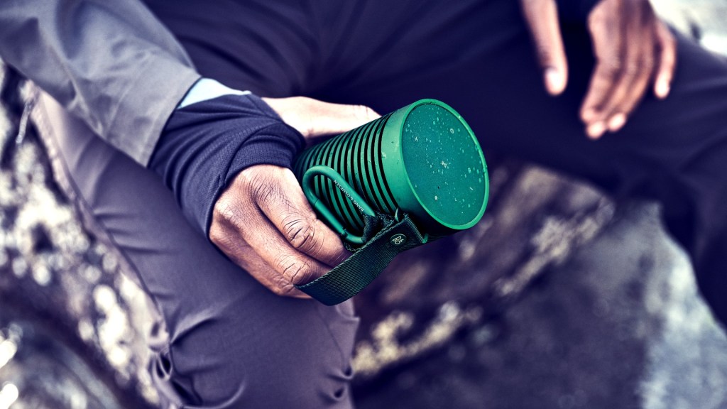 The Beosound Explore portable speaker held on a rocky outcrop
