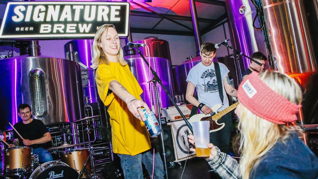 As a band plays on stage, the singer hands out a can of beer to an audience member