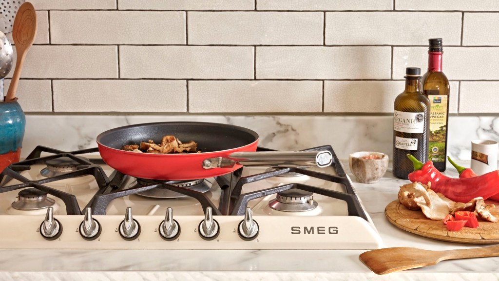Red Smeg frying pan on a cooker surrounded by ingredients