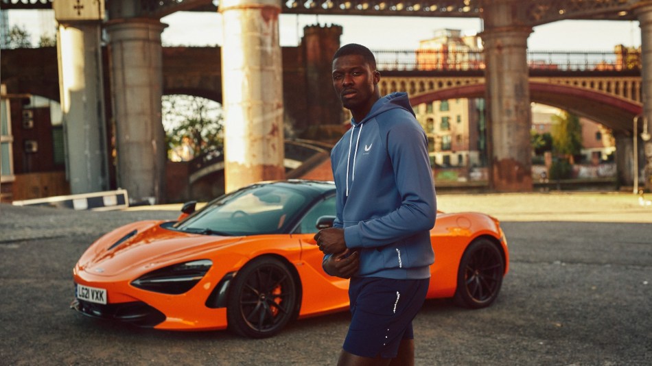 Athletic man stands in front of a McLaren supercar wearing Castore McLaren sportwear