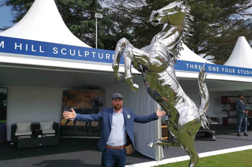 Sculptor Tom Hill at Salon prive in front of a big metal horse