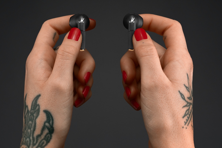 Marshall Minor III earbuds held in a pair of tattooed hands