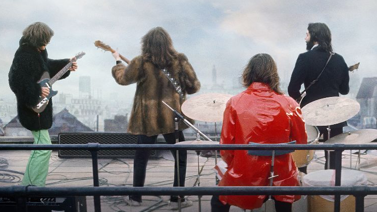 The Beatles, photographed from behind, as they perform on the Apple Corps rooftop in 1969