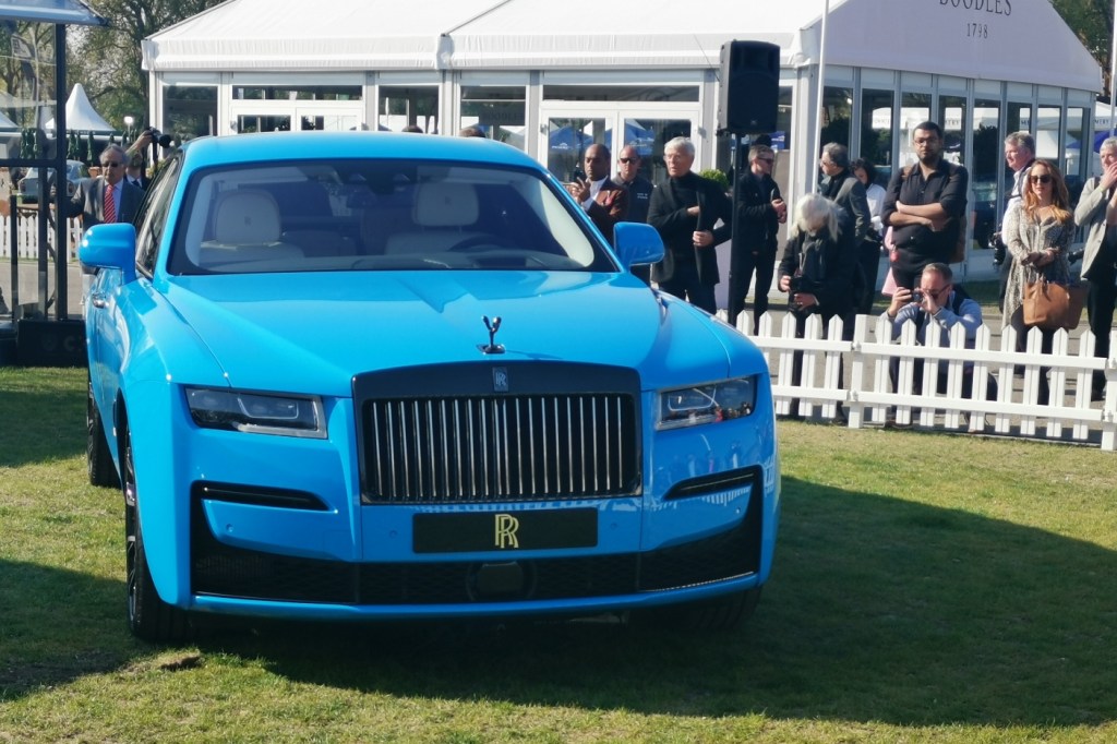 The Rolls-Royce Black Badge Ghost is blue, sits on a white-fenced lawn at Salon Prive