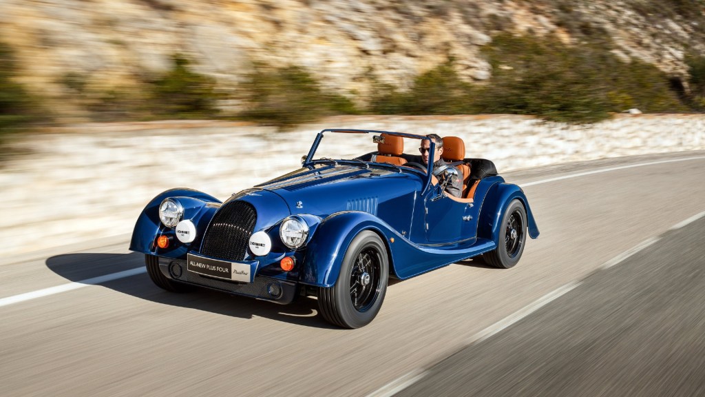 A Morgan Plus Four sports car roars along a country road