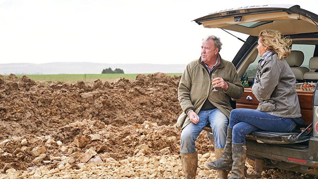 Jeremy Clarkson sits on the back of a 4x4 looking over his farm, glass of wine in hand