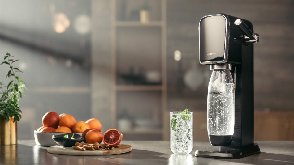 The SodaStream Art on a kitchen table with a glass of fizzy water