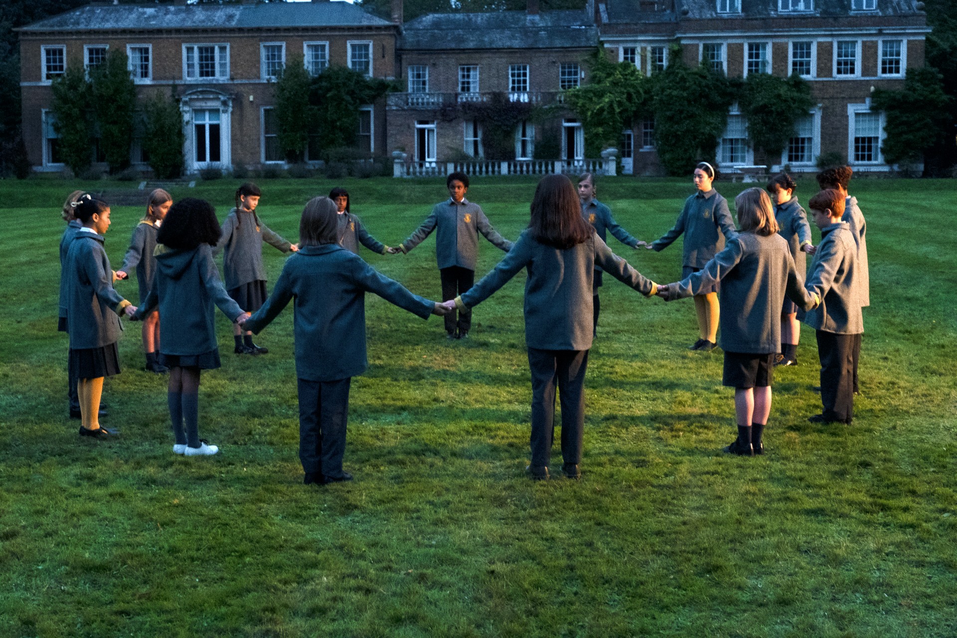 A ring of creepy kids gather on the grounds outside their school in in The Midwich Cuckoos