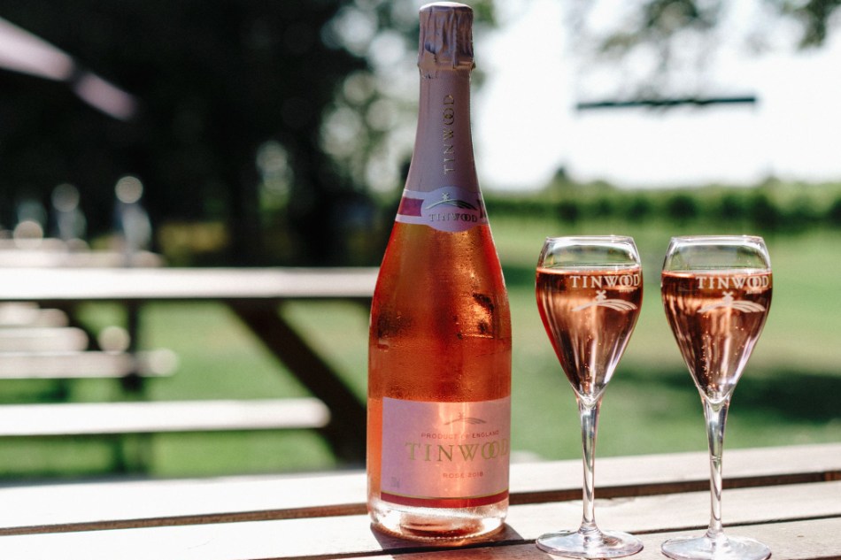 A bottle of Tinwood Estate sparkling rose and two glasses, glinting in the summer sun
