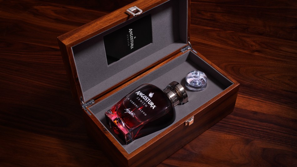A bottle of Angostura Zenith Rum Caroni Blend rests elegantly in a wooden presentation box, the grey fabric contrasting with the rich hues of the liquid inside