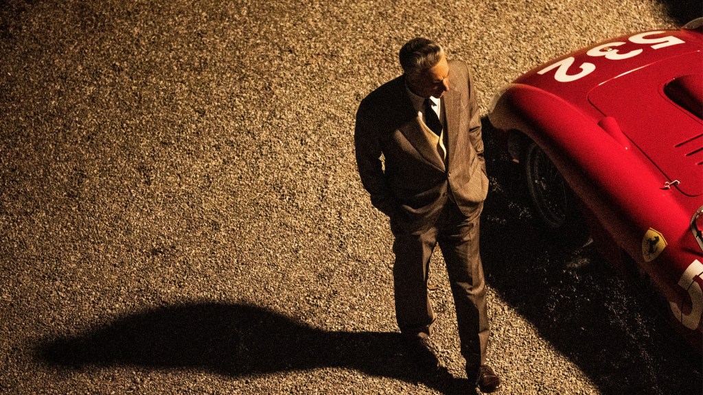 Adam Driver as Enzo Ferrari walks around a bright red racing car