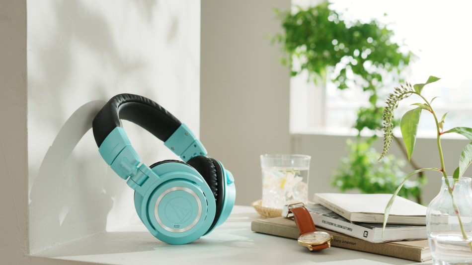 Audio Technica Ice Blue Bluetooth M50x headphones in a window alongside books and a watch