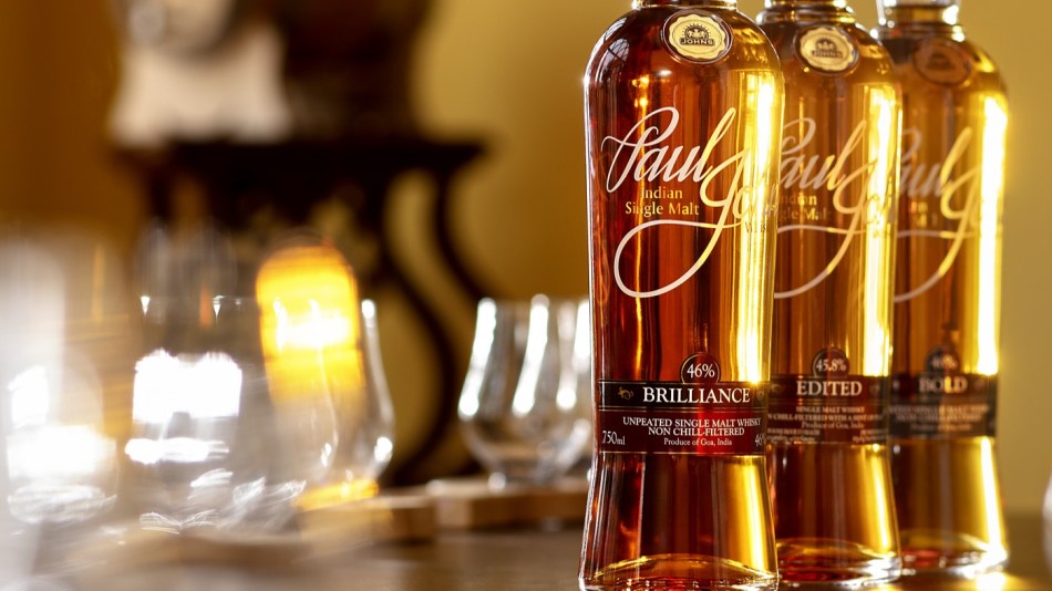 Paul John whiskies on a bar with glasses in the background