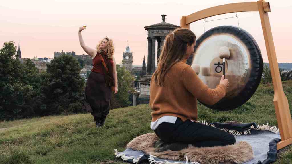 Madeleine Schmoll of The Scotch Malt Whisky Society rasing a toast to the start of whisky season on Calton Hill, Edinburgh, with Jo McCoy of Blissness, a gong sound bath practitioner