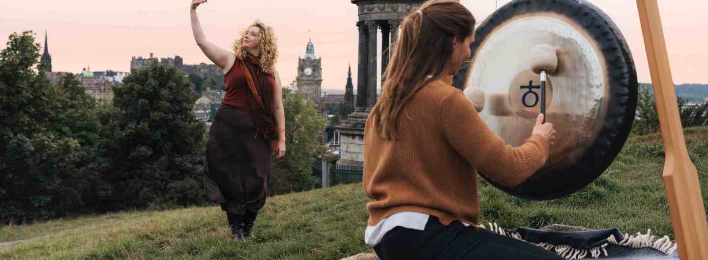 Madeleine Schmoll of The Scotch Malt Whisky Society rasing a toast to the start of whisky season on Calton Hill, Edinburgh, with Jo McCoy of Blissness, a gong sound bath practitioner